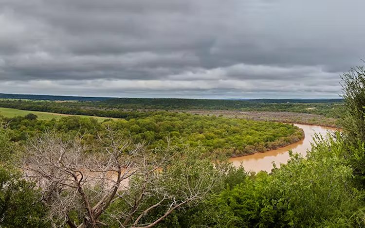 Gran extensión de tierra con árboles, campos y cuerpo de agua.